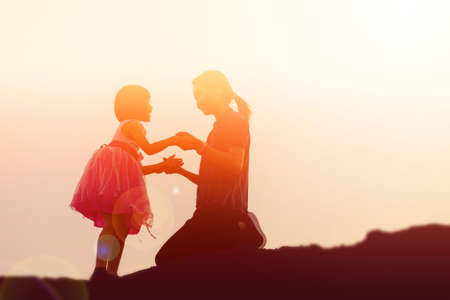 Mother encouraged her daughter out of the shadows at sunset.の写真素材