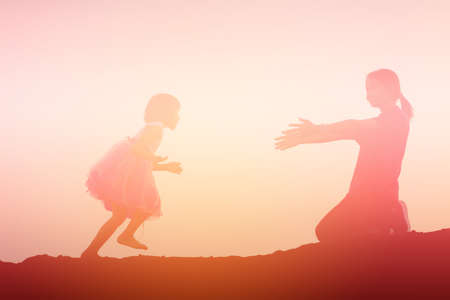 Mother encouraged her daughter out of the shadows at sunset.の写真素材