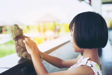 Little child girl is reading a book in evening in dark with a toy bear stock photoの写真素材
