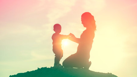 Mother encouraged her son outdoors at sunset, silhouette conceptの写真素材