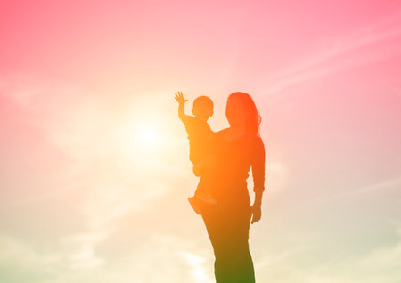 Mother encouraged her son outdoors at sunset, silhouette conceptの写真素材