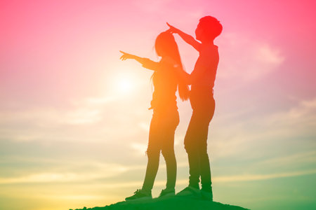 silhouette of happy young couple pointing finger on sunset sky backgroundの写真素材