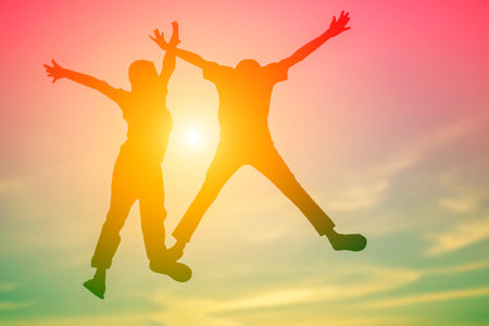 Silhouette of happy young couple jumping at sunset sky background.