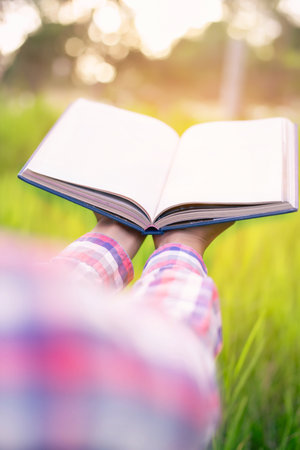Happy woman lying on green grass reading a book in the park (outdoors)の写真素材