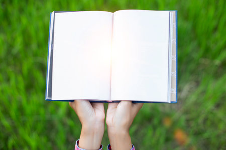 Happy woman lying on green grass reading a book in the park (outdoors)の写真素材