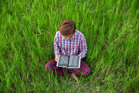 Happy woman lying on green grass reading a book in the park (outdoors)