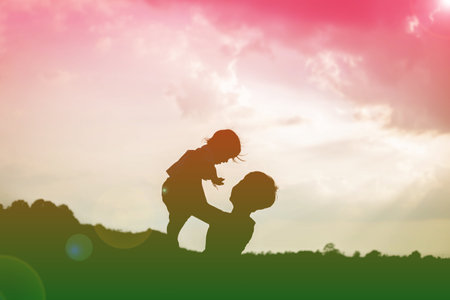 A silhouette of a happy young mother harmonious family outdoors. laughing and playing in the summer on the sunset background.SSTKhomeの写真素材