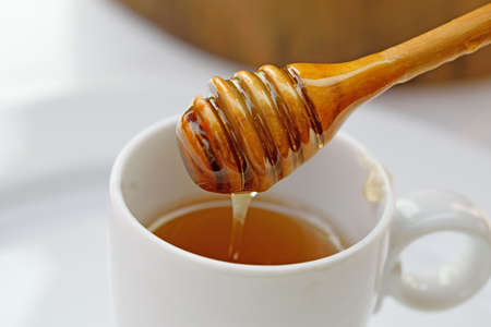 Honey dripping from wooden spoon into the Cupの写真素材