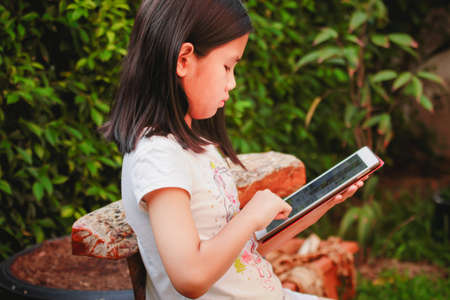 Little girl playing on tablet pc at gardenの写真素材