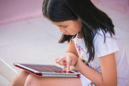 Little girl playing on tablet pc at gardenの写真素材