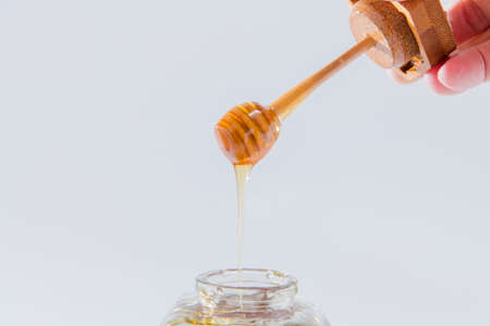Honey dripping from wooden honey dipper on white backgroundの写真素材