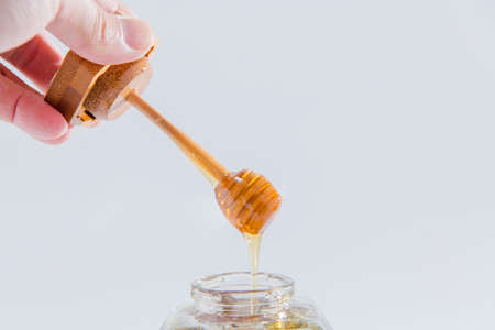Honey dripping from wooden honey dipper on white backgroundの写真素材