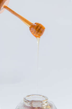 Honey dripping from wooden honey dipper on white backgroundの写真素材