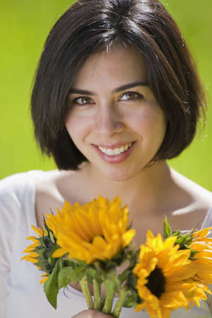 beautiful, young Hispanic woman in a grassy meadow holding flowersの写真素材