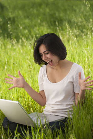 beautiful, young Hispanic woman working on a laptop computer in a grassy meadowの写真素材
