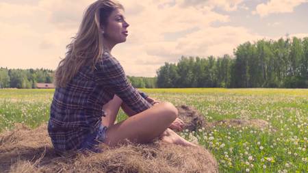 Young woman sitting on haystack at summerの写真素材