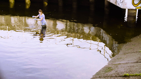 Ecologist getting samples of plants in city riverの写真素材