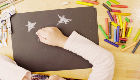 A girl drawing pastel crayons on paper at a table in a roomの写真素材