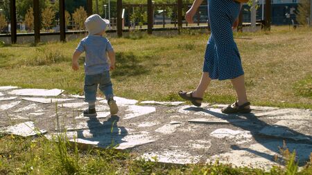 Baby boy walking along the road in the park. His mom walking after him.の写真素材