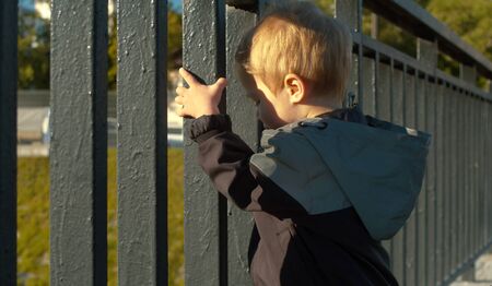 Little boy standing near the fence in the city. Side viewの写真素材