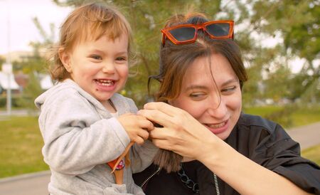 Glad little girl sitting on mom's hands and laughingの写真素材