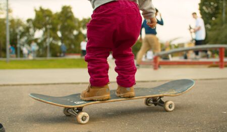 Legs of funny baby standing on a skate and trying to ride. Blurry unrecognizable people riding a skates in slow motionの写真素材