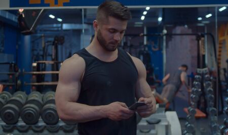 Athlete during the break looking in smart phone. Bodybuilder in the gymの写真素材