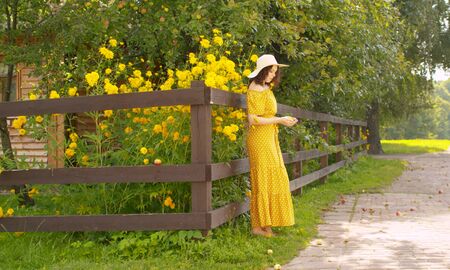 Young romantic woman standing near the courtyard of a village house on a background of flowers. Rural sceneの写真素材