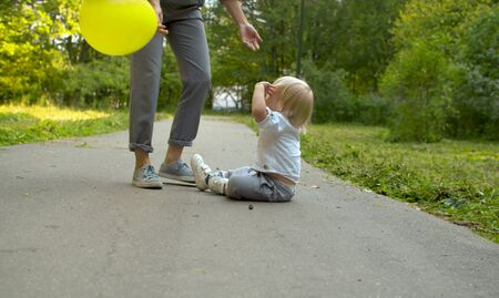 Unhappy toddler sitting on the road. Mother and her son in the park