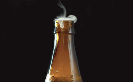 Close up open bottle of beer on black background. Foam and bubbles begin to rise in the bottle and gas escapes from the neck.の写真素材