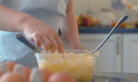 Close up hand of child tasting dough. Children cooking pastries in bright kitchenの写真素材