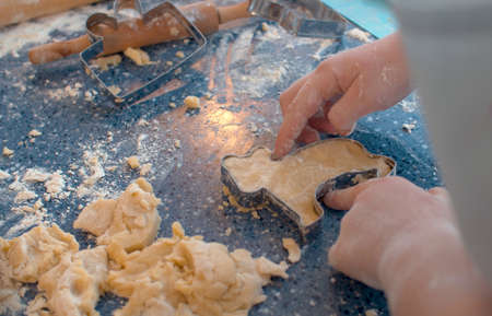 Close up hands of a girl making cookies with a cookie cutter. Children cooking pastry in bright kitchenの写真素材