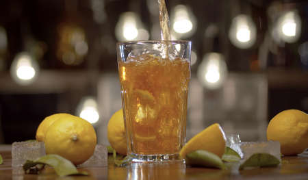 Close up tea pouring into the glass with ice and lemon. Glass with ice tea or cocktail, ice, lemons...