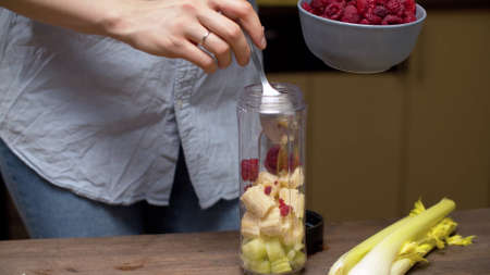 Female hands pouring raspberries in blender glass with banana and celery slices. Healthy lifestyle and eating conceptの写真素材