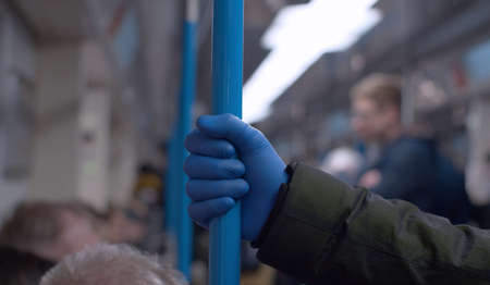 Close up hand in protective glove holds grab bar in subway car. Man in subway during coronavirus epidemic. Safety lifestyle concept. COVID-19 pandemicの写真素材