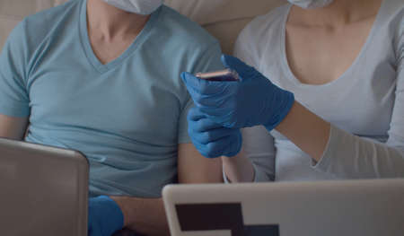 Close up female hands in protective blue gloves holding smart phone. The wife shows something to her...