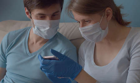 An alarmed couple looking for news on a coronavirus in a smartphone. The wife finds something. She is very surprised and shows her husband. Quarantine, coronavirus epidemic.の写真素材
