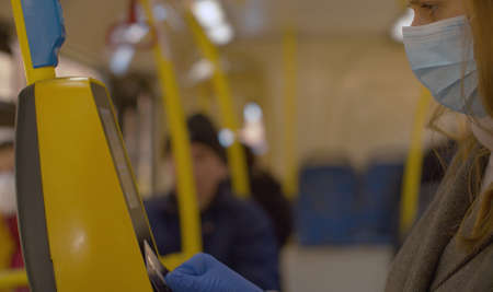 Close up woman in protective mask and gloves paying in the bus. She pays for fare with an electronic...