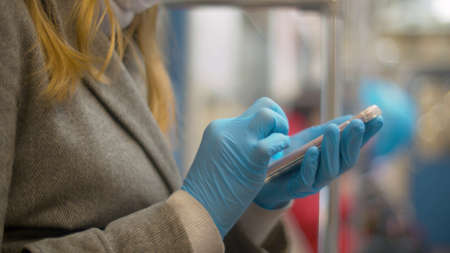 Close up female hand in blue protective glove typing in the smart phone during the trip in subway....
