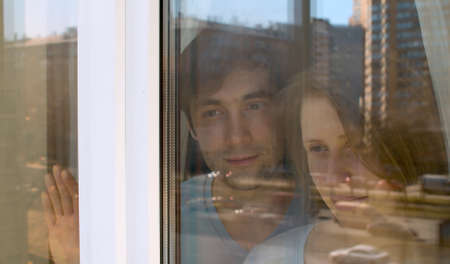 Young happy couple in love shooting through the window. They are looking outside. The window...