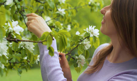 Close up profile portrait of beautiful woman in the garden near apple tree in blossom. She is...
