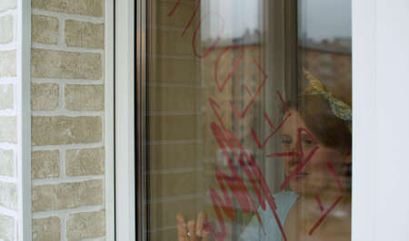 Young beautiful woman writing word Freedom on the window glass using lipstick. The end of...