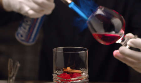 Making of Raspberry Sambuca. Close up barmans hand sets fire to sambuca in snifter.