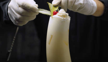 Close up bartenders hands garnishing Pina Colada Cocktail with whipped cream and pineapple leaves.の写真素材