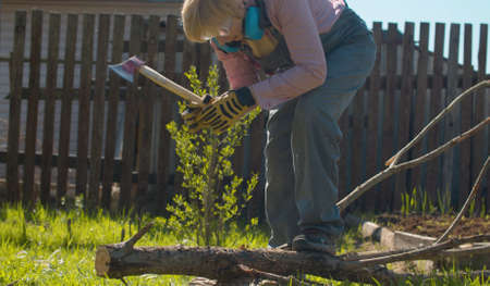 Mature woman chopping branches of a tree with ax in the yard of a country house. Active and healthy lifestyle conceptの写真素材
