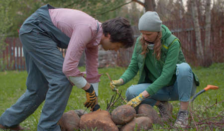 Couple breaking a tree branches for a bonfire. Young handsome family prepares brushwood to light a bonfire in the yard of a country house. People activity and healthy lifestyle conceptの写真素材