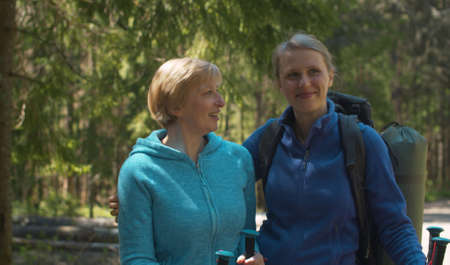 Close up portrait of young handsome woman with her mother in the forest. They are hugging, talking and smiling. Trekking in the forest, active and healthy lifestyle conceptの写真素材