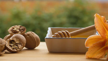 Close up honey spoon in a bowl with honey. Walnuts and lily on a table outdoors. Healthy fresh food...
