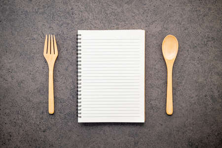 Notebook with wooden spoon set up on dark stone background.