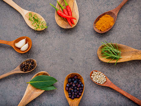 Various of spices and herbs in wooden spoons. Flat lay spices ingredients chili ,peppercorn, rosemary, thyme on dark stone background.の写真素材